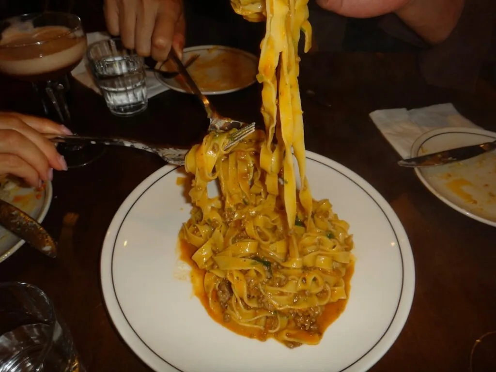 Gabeln und Hände teilen frische Tagliatelle mit Fleischsauce am Tisch