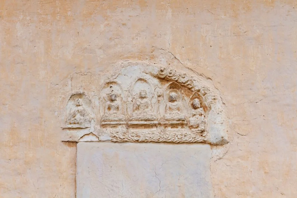 Bas-relief ancien encastré dans un mur ocre, détails de figures.