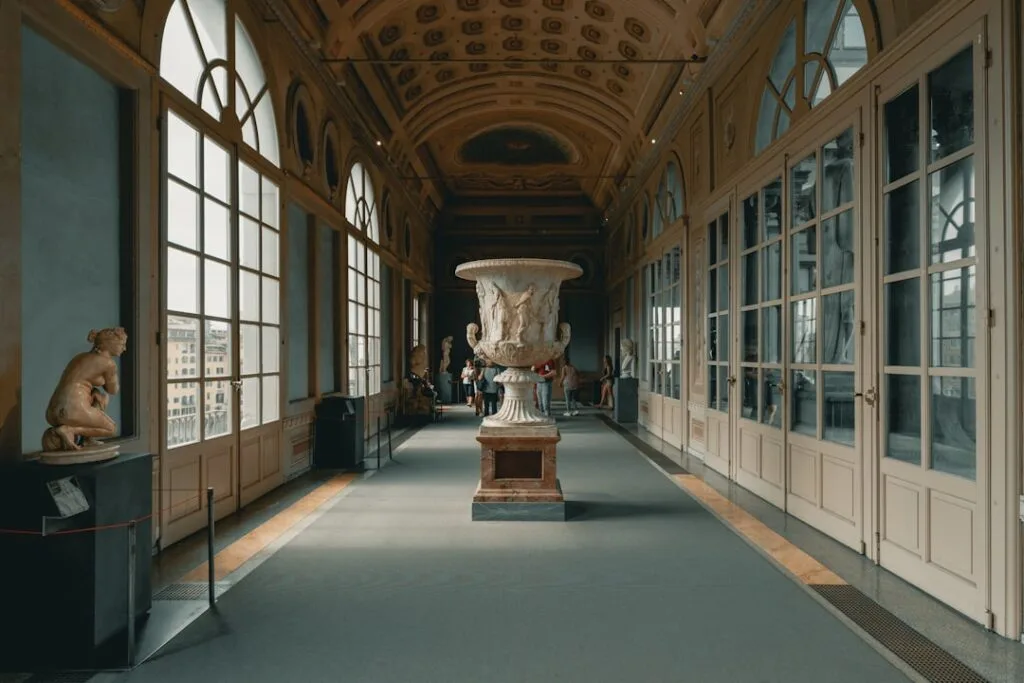 Langer Museumsflur mit zentraler Marmorvase und Fenstern auf Florenz