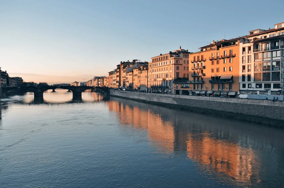 Fluss Arno mit Gebäudereflektionen und Brücke in Florenz bei Sonnenuntergang