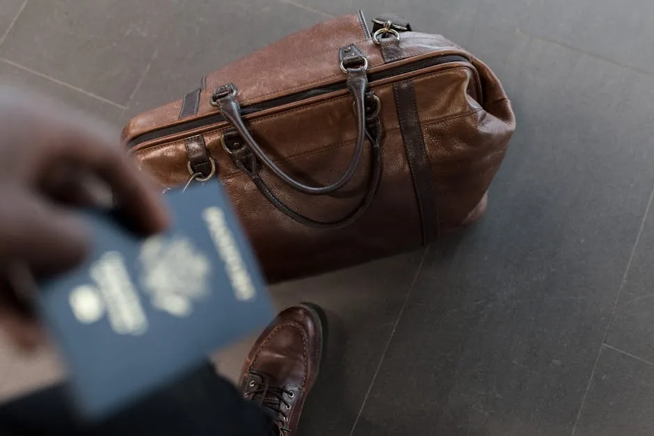 Sac de voyage en cuir brun posé au sol près d'un passeport