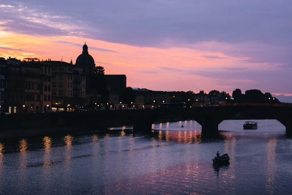 Abendlicher Blick auf den Arno mit Booten und Brücke in Florenz