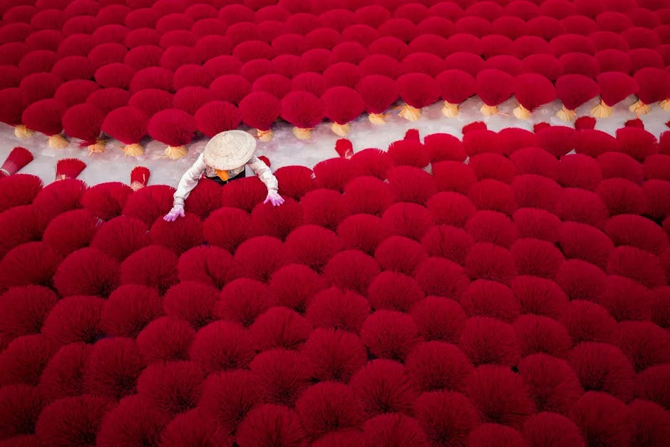 Personne au chapeau conique manipulant des bouquets d'encens rouges séchant.