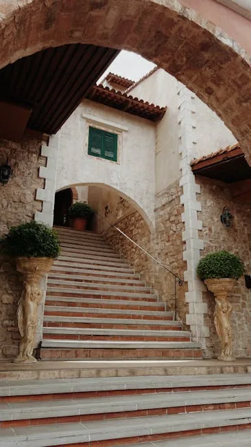Escalier voûté encadré par deux atlantes et pots de verdure.