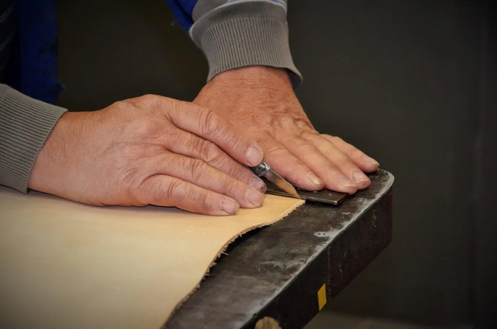 Mains coupant une pièce de cuir beige sur une table d'atelier à Florence