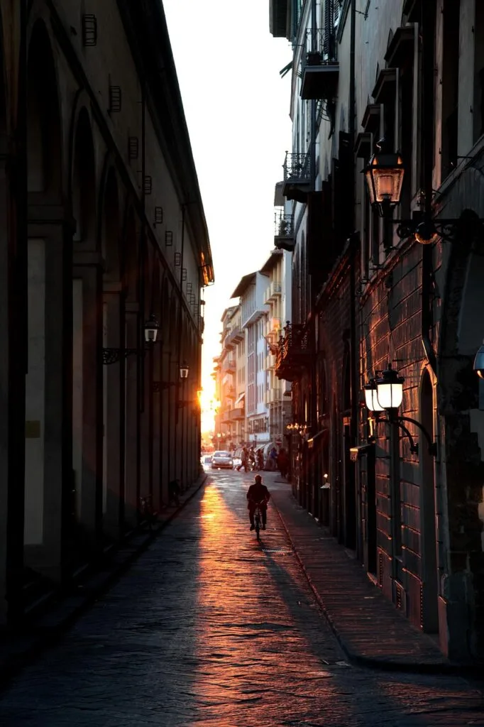 Ruelle florentine au coucher de soleil, cycliste silhouetté vers l'horizon.